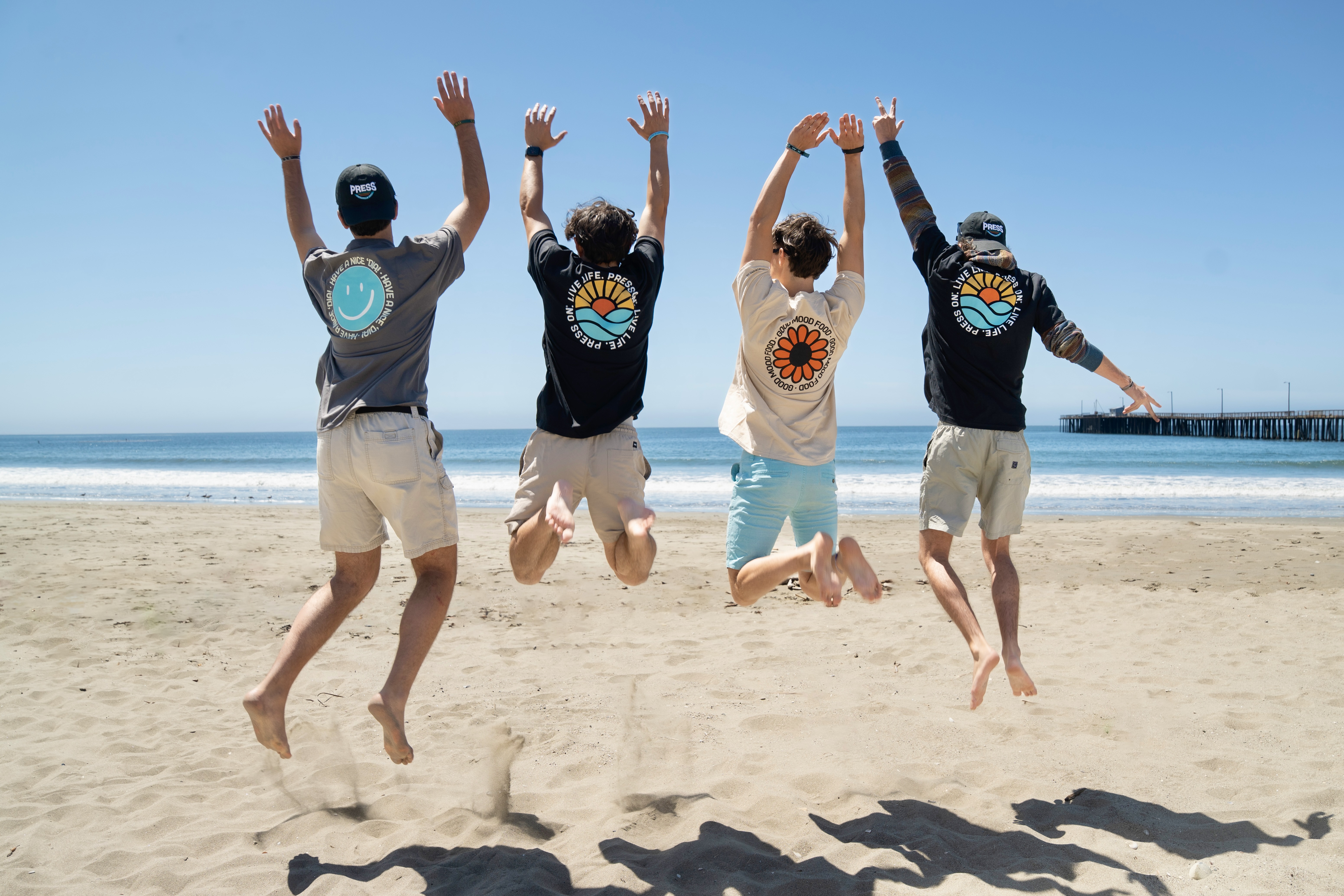 Four people jumping on the beach with their hands up.