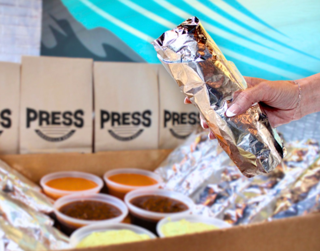 Woman holding a wrapped Press Quesadilla Grill Catering burrito with the Burrito Box in the background