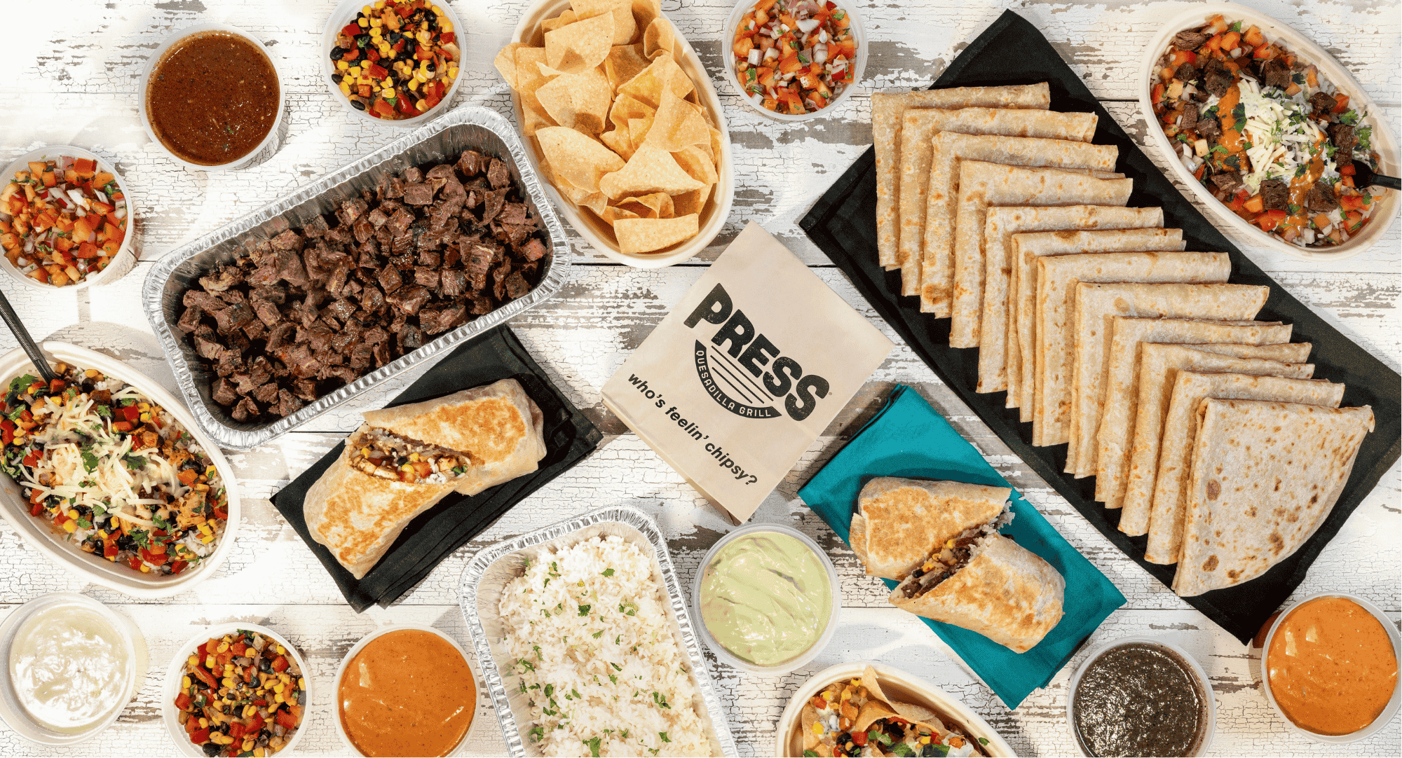 A catering spread consisting of burritos, chips, salsa and more