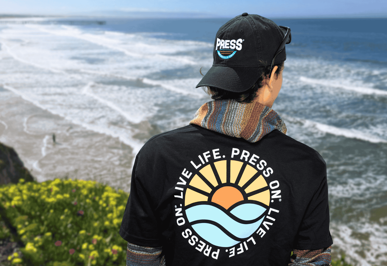 A young man wearing a Press hat and t-shirt looking at the coastline in California. 