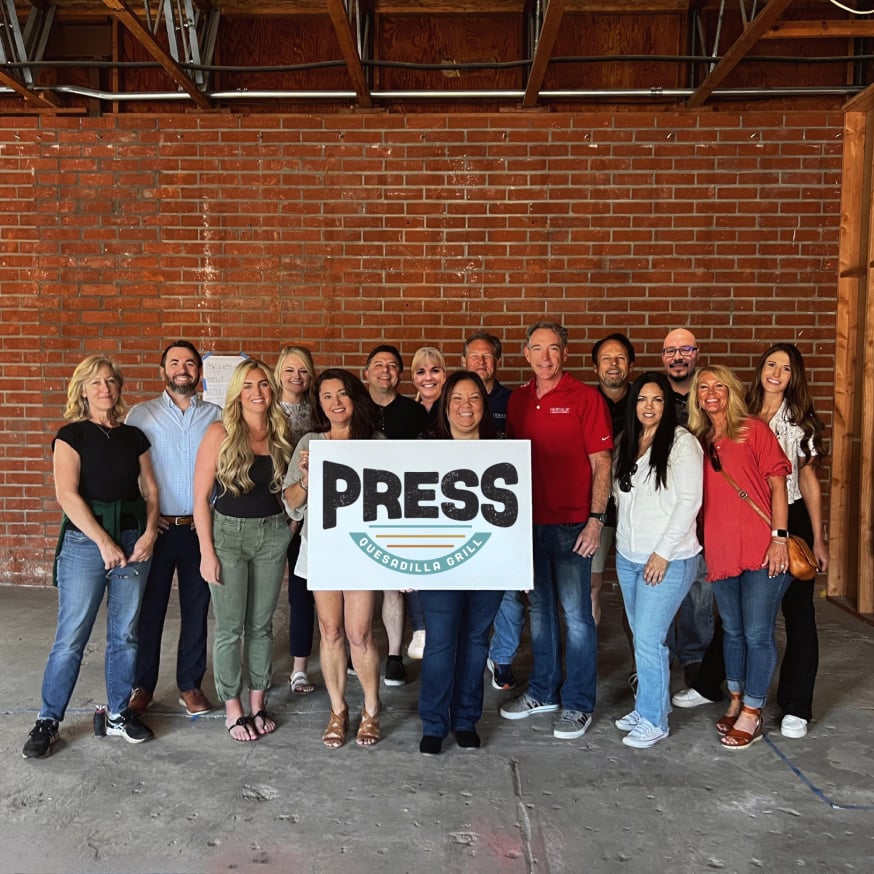 Many people standing together while holding a sign that has the Press logo.