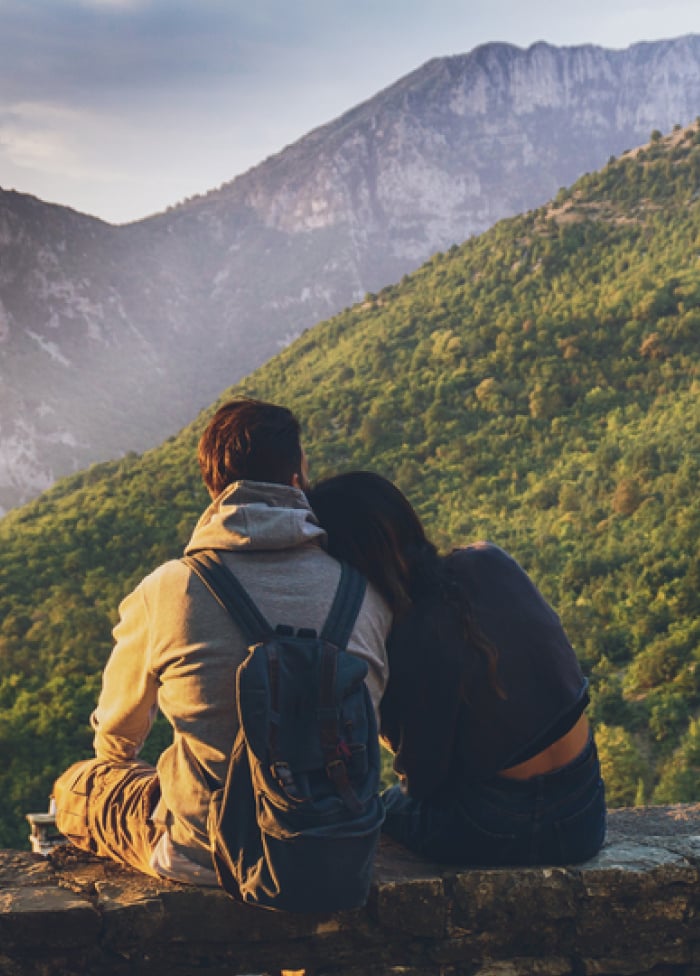 Two people sitting on a concrete wall looking out into the mountains.