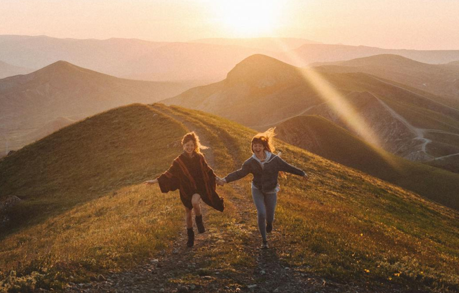 Two smiling people running on a hill while holding hands.