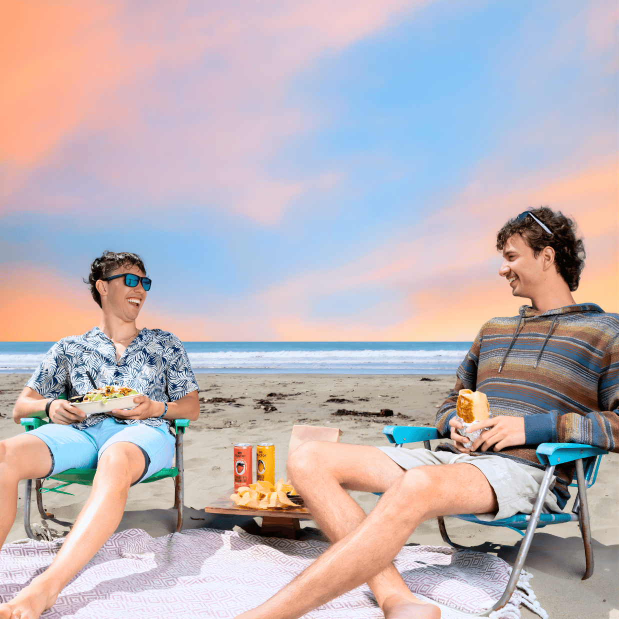 Two male friends laughing on the beach with a Press protein bowl and burrito.